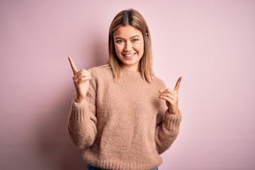 Young beautiful blonde woman wearing winter wool sweater over pink isolated background smiling confident pointing with fingers to different directions. Copy space for advertisement
