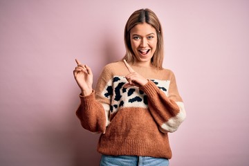 Young beautiful blonde woman wearing fashion animal print sweater over pink background smiling and looking at the camera pointing with two hands and fingers to the side.