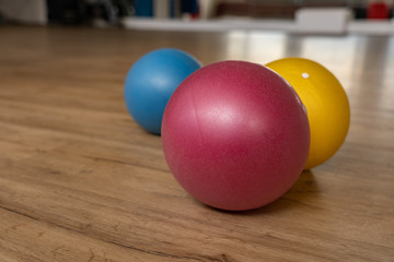 Three small and colorful gymnastic balls on wooden floor of a gymnastic hall of a group fitness center.