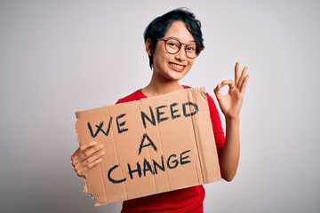Beautiful asian girl protesting holding banner with change message over white background doing ok sign with fingers, excellent symbol