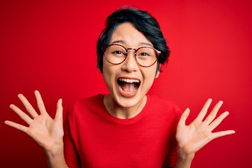 Young beautiful asian girl wearing casual t-shirt and glasses over isolated red background...
