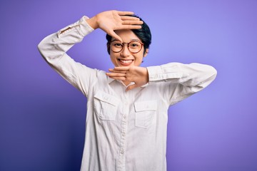 Young beautiful asian girl wearing casual shirt and glasses standing over purple background Smiling cheerful playing peek a boo with hands showing face. Surprised and exited