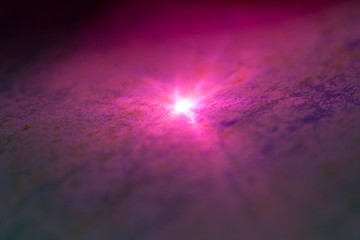 imagen cósmica con destello de luz central sobre textura con tonos rosados y morados