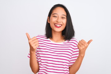 Young chinese woman wearing striped t-shirt standing over isolated white background success sign doing positive gesture with hand, thumbs up smiling and happy. Cheerful expression and winner gesture.