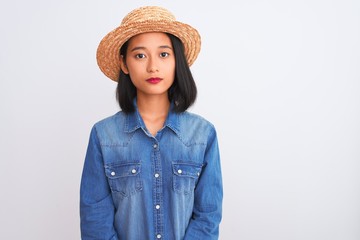 Young beautiful chinese woman wearing denim shirt and hat over isolated white background with serious expression on face. Simple and natural looking at the camera.