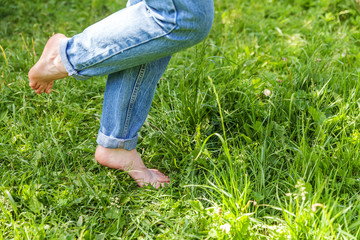 Naklejka na ściany i meble Two beautiful female feet walking on grass in sunny summer morning. Light step barefoot girl legs on soft spring lawn in garden or park. Healthy freedom relax concept.