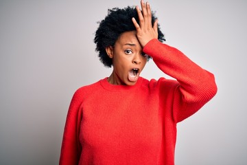 Young beautiful African American afro woman with curly hair wearing red casual sweater surprised...