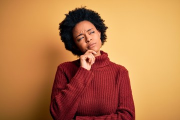 Fototapeta na wymiar Young beautiful African American afro woman with curly hair wearing casual turtleneck sweater with hand on chin thinking about question, pensive expression. Smiling with thoughtful face. Doubt 