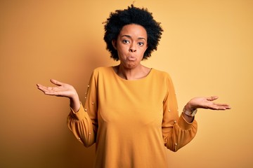 Young beautiful African American afro woman with curly hair wearing casual t-shirt clueless and...