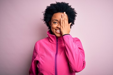 Fototapeta na wymiar Young African American afro sportswoman with curly hair wearing sportswear doin sport covering one eye with hand, confident smile on face and surprise emotion.