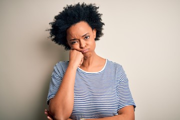 Young beautiful African American afro woman with curly hair wearing striped t-shirt thinking...