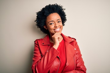 Fototapeta na wymiar Young beautiful African American afro woman with curly hair wearing casual red jacket looking confident at the camera with smile with crossed arms and hand raised on chin. Thinking positive.