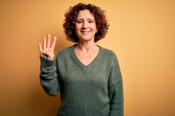 Middle age beautiful curly hair woman wearing casual sweater over isolated yellow background showing and pointing up with fingers number four while smiling confident and happy.