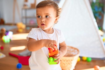 Adorable toddler playing with building blocks around lots of toys at kindergarten