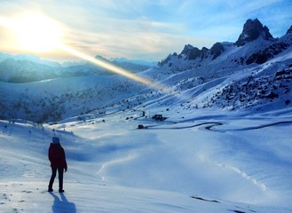 View of the Dolomites in the winter at sunset from the height of the Jau Pass in Italy. A man stands looking at the mountains, around a lot of snow.