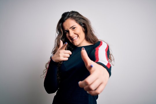 Young beautiful woman with curly hair wearing casual sweater over isolated white background pointing fingers to camera with happy and funny face. Good energy and vibes.