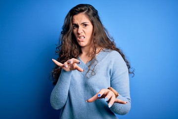 Young beautiful woman with curly hair wearing blue casual sweater over isolated background disgusted expression, displeased and fearful doing disgust face because aversion reaction.