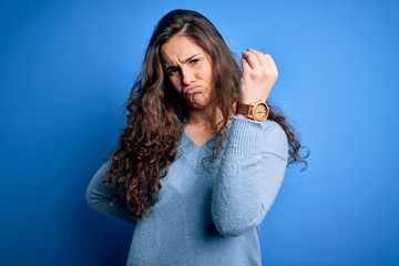 Young beautiful woman with curly hair wearing blue casual sweater over isolated background Doing Italian gesture with hand and fingers confident expression