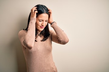 Young brunette woman with blue eyes wearing casual sweater over isolated white background suffering from headache desperate and stressed because pain and migraine. Hands on head.