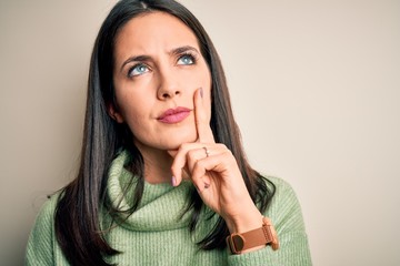 Young brunette woman with blue eyes wearing turtleneck sweater over white background serious face...