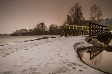 Drweniany mały mostek na zamarźniętym jeziorze w mroźny zimowy wieczór