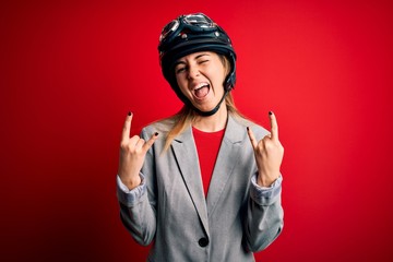 Young beautiful blonde motorcyclist woman wearing motorcycle helmet over red background shouting...