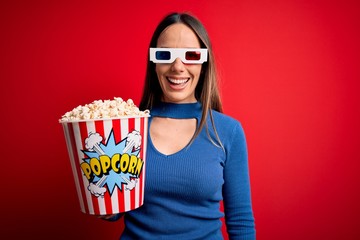 Young blonde woman wearing 3d glasses and eating pack of popcorn watching a movie on cinema winking...