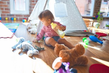 Adorable toddler holding feeding bottle around lots of toys at kindergarten