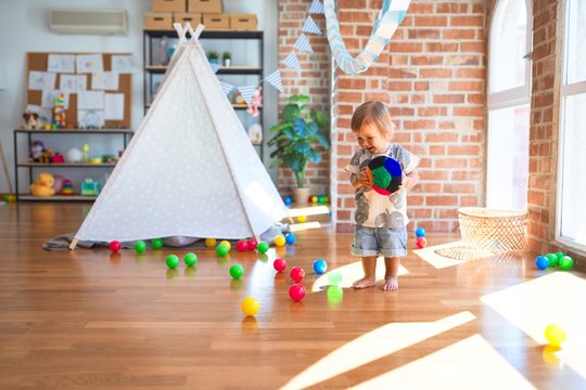 Adorable toddler playing with balls around lots of toys at kindergarten