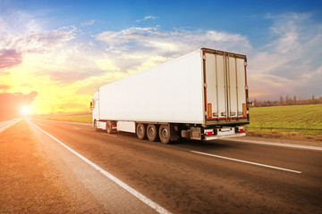 A big truck and a trailer on the countryside road against a sky with a sunset