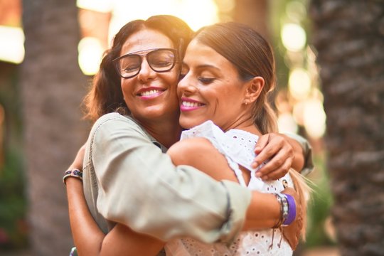 Beautiful mother and daughter smiling happy and confident. Standing with smile on face hugging at town park