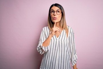 Young beautiful woman wearing casual striped t-shirt and glasses over pink background Thinking...