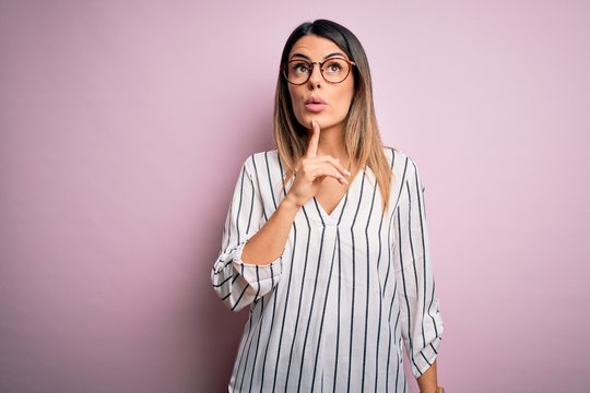 Young beautiful woman wearing casual striped t-shirt and glasses over pink background Thinking concentrated about doubt with finger on chin and looking up wondering