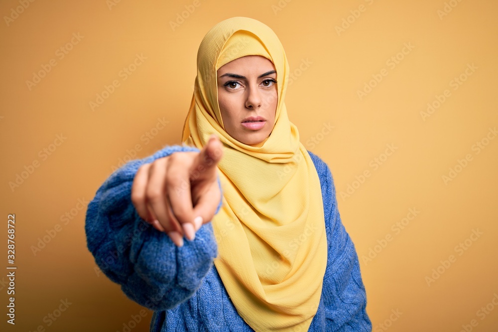 Poster young beautiful brunette muslim woman wearing arab hijab over isolated yellow background pointing di