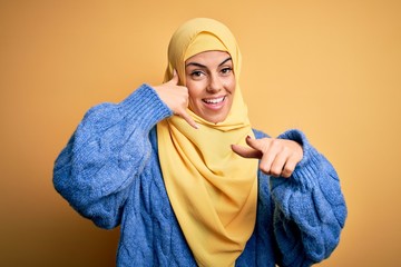 Young beautiful brunette muslim woman wearing arab hijab over isolated yellow background smiling...