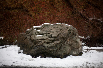 Giant stone in the snow. Natural background with a stone. Minimalism in nature. Strong base. A piece of rock on the road. Calm rock. Meditation of nature.
