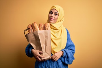 Young beautiful brunette arab woman wearing islamic hijab holding paper bag with bread with a confident expression on smart face thinking serious