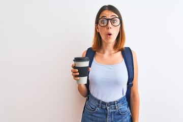 Beautiful redhead student woman wearing a backpack and drinking take away coffee scared in shock with a surprise face, afraid and excited with fear expression