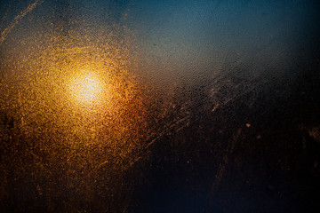 Fototapeta na wymiar Cloudy glass in warm and cold colors. Dawn behind a blurry transparent surface. Abstract warm background. The texture of the glass is condensed. The soft light of the morning sun on a rough surface.
