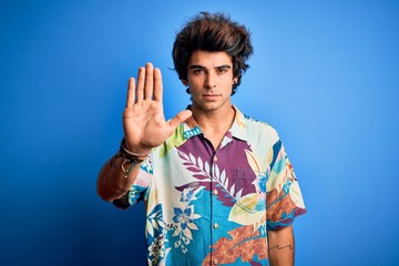 Young handsome man on vacation wearing summer shirt over isolated blue background doing stop sing...
