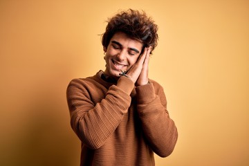 Young handsome man wearing casual shirt and sweater over isolated yellow background sleeping tired dreaming and posing with hands together while smiling with closed eyes.