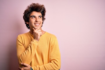 Fototapeta na wymiar Young handsome man wearing yellow casual t-shirt standing over isolated pink background with hand on chin thinking about question, pensive expression. Smiling with thoughtful face. Doubt concept.