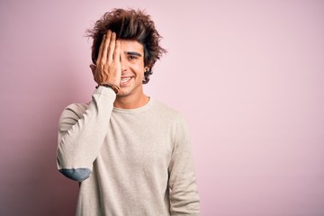 Fototapeta na wymiar Young handsome man wearing casual t-shirt standing over isolated pink background covering one eye with hand, confident smile on face and surprise emotion.