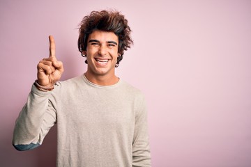 Young handsome man wearing casual t-shirt standing over isolated pink background pointing finger up with successful idea. Exited and happy. Number one.