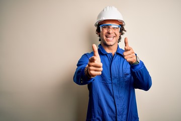 Young constructor man wearing uniform and security helmet over isolated white background pointing fingers to camera with happy and funny face. Good energy and vibes.