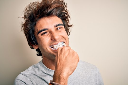 Young handsome man smiling happy. Standing with smile on face whasing tooth using toothbrush over isolated white background