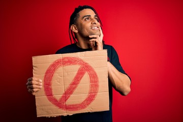 Young handsome african american man with dreadlocks holding banner with prohibited signal serious...