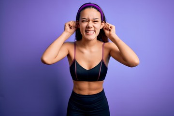 Fototapeta na wymiar Young beautiful sporty girl doing sport wearing sportswear over isolated purple background Smiling pulling ears with fingers, funny gesture. Audition problem