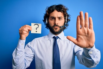Young call center agent man with beard working using headset holding question mark reminder with open hand doing stop sign with serious and confident expression, defense gesture