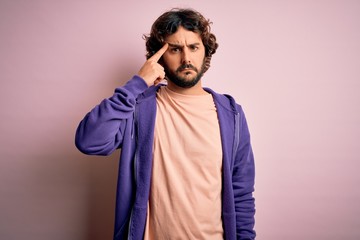 Young handsome sporty man with beard wearing casual sweatshirt over pink background pointing...